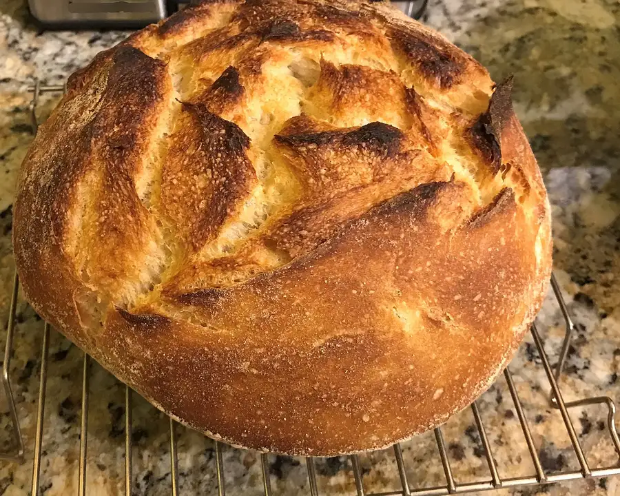 Miche au levain à la croûte dorée et grignée, posée sur une grille de refroidissement